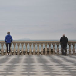 Rear view of people standing on retaining wall by sea