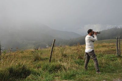 Rear view of man standing on mountain during foggy weather