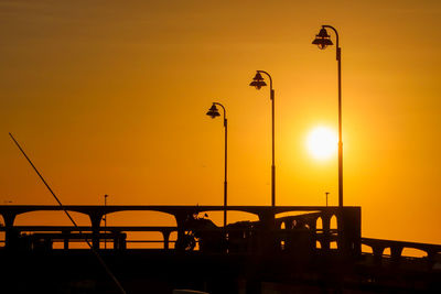 Silhouette wooden pier lights against orange sky during sunset