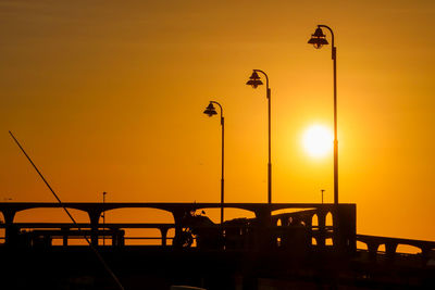 Silhouette street lights against orange sky during sunset