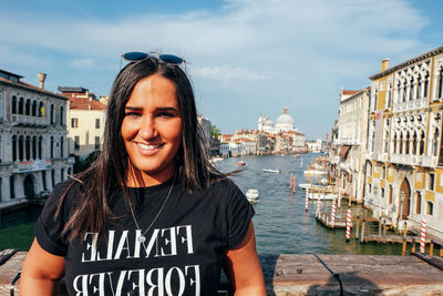 Portrait of smiling young woman standing against buildings in city