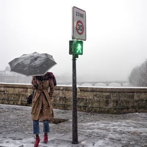 Woman with umbrella standing against sky during winter