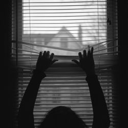 Silhouette woman holding blinds on window at home