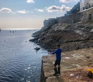 Man standing on rock by sea against sky