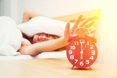 Young woman hand reaching towards alarm clock while sleeping on bed at home