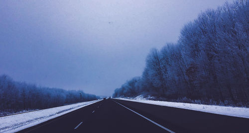Road amidst trees against sky during winter