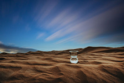 View of drinking glass on sand against sky