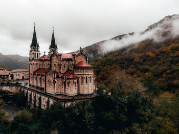 Historic basilica by mountain against cloudy sky