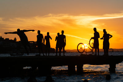 Young people and silhouettes are seen together during sunset having fun on top of the crush bridge
