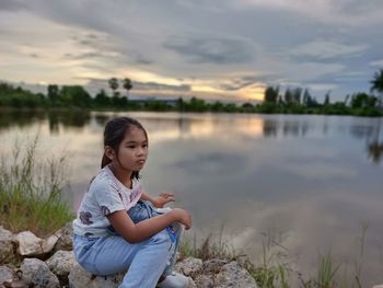 Girl sitting by lake against sky