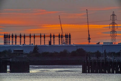 Silhouette of wooden posts by sea against sky during sunset