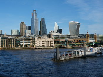 Modern buildings by river against sky in city