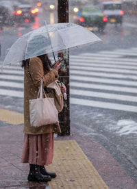 Woman with umbrella standing on sidewalk during winter