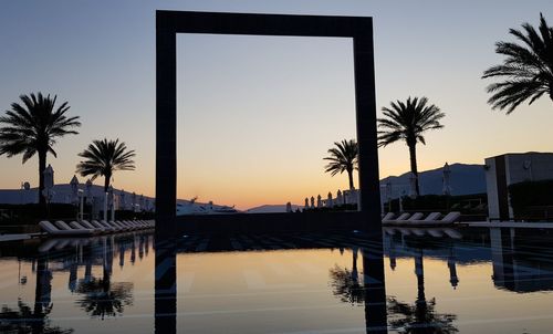 Palm trees by swimming pool against sky during sunset