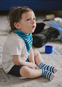 Close-up of cute baby wearing bib and socks and looking with surprise at the television 