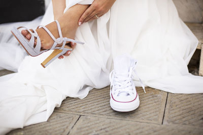 Detail of a bride who her elegant shoes with comfortable sneakers while sitting on a sidewalk