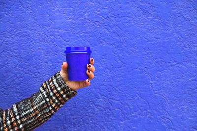 Close-up of person holding blue coffee cup against blue wall