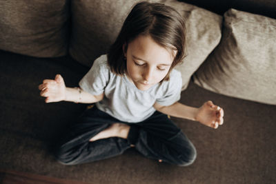 The girl is sitting at home on the sofa, yoga in the lotus position. relaxation and tranquility