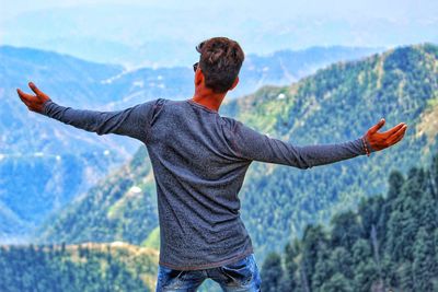 Rear view of man with arms outstretched standing on mountain