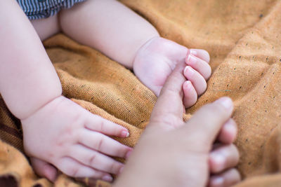 Cropped image of mother holding baby hand on blanket
