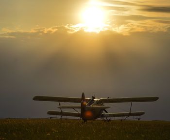 Airplane flying over field against sky during sunset