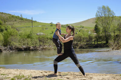 Smiling mid adult woman exercising with son by river