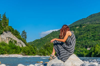 Man sitting on mountain against blue sky