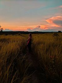 Side view of woman on field against sky during sunset