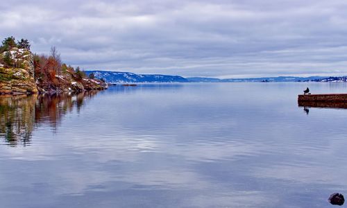 A reflected rocky beach and a lone fisherman