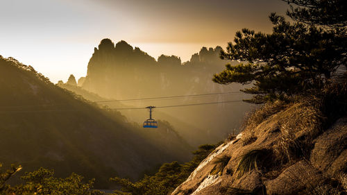 Overhead cable car hanging against mountain during sunset