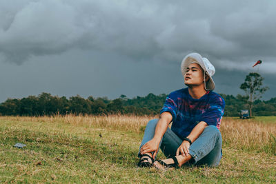 Young man looking away while sitting on land