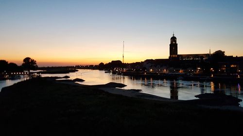 Silhouette of buildings by river during sunset