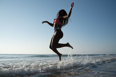 Black woman with braids on the beach jumping on the beach