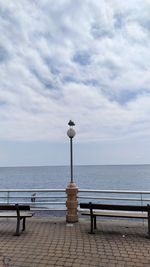 Bench on railing by sea against sky