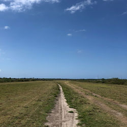 Road passing through field against sky