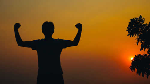 Rear view of silhouette man standing against orange sky