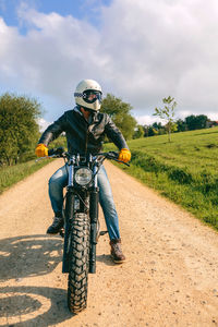 Man riding motorcycle on dirt road against sky