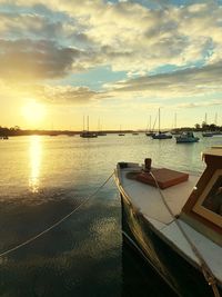 Sailboats moored at harbor against sky during sunset