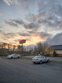 Cars parked on road against sky during sunset