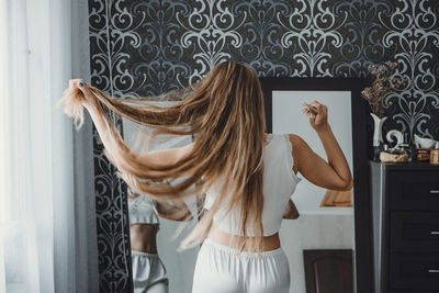 Rear view of woman combing hair at home