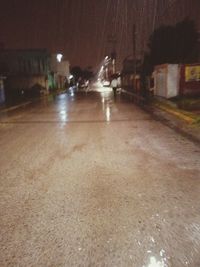 Wet street amidst illuminated buildings in city at night