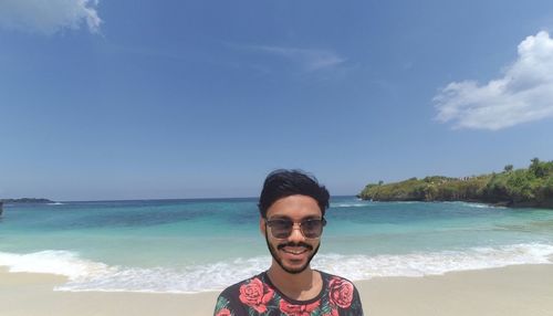 Portrait of young man standing at beach against sky