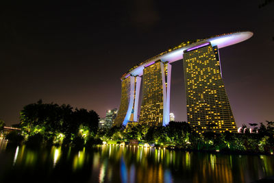 Illuminated building by lake against sky at night