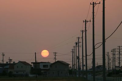 Power lines by houses against sky during sunset