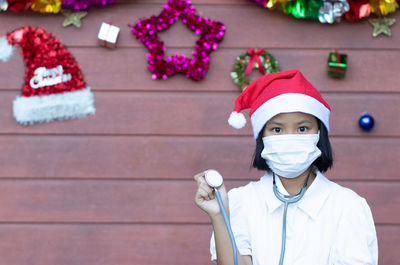 Portrait of girl wearing lab coat while standing against christmas decorations on wall