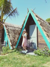 Woman standing by beach hut against clear sky during sunny day