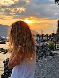 Side view of woman standing at beach against sky during sunset