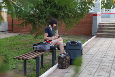 A happy brunette woman is sitting on a bench at the train station