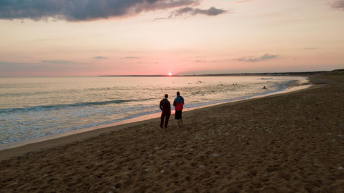 People on beach against sky during sunset