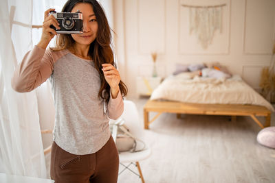 Young woman holding retro camera in room